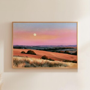 May include: A landscape painting in a wooden frame depicting a vast field of golden grass under a soft pink and blue sunset sky. A pale yellow moon is visible in the upper centre. The horizon features rolling hills and dark green trees.