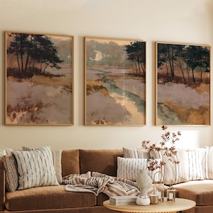May include: A set of three framed wall art prints depicting a landscape with dark trees, a winding stream, and muted earth tones of brown, tan, and soft green. The artwork features a fox in the centre panel and is displayed in light wood frames.