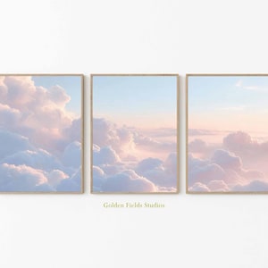 Puede incluir: Tres impresiones enmarcadas que muestran un cielo pastel lleno de nubes rosadas y blancas. La obra de arte está sobre un cielo azul claro, creando una atmósfera serena y soñadora. El texto "Golden Fields Studios" es visible.