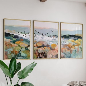 May include: A triptych of framed art prints. Each print depicts a watercolour landscape with colourful flowers, mountains, and birds. The frames are gold-coloured. The artwork is suitable for a living room or bedroom.