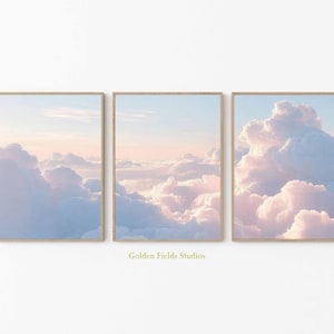 Puede incluir: Tres impresiones artísticas enmarcadas que representan una serena escena del cielo con nubes de colores pastel. La obra de arte muestra un degradado de suaves azules, rosas y blancos, creando una atmósfera tranquila y etérea. Los marcos son de color madera clara, y el texto "Golden Fields Studios" es visible.
