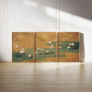May include: A triptych of framed art panels. Each panel features a gold background with a green and gold water scene. White flowering branches are depicted, with a few red fish. The frames are gold, and the artwork is displayed on a wood floor.