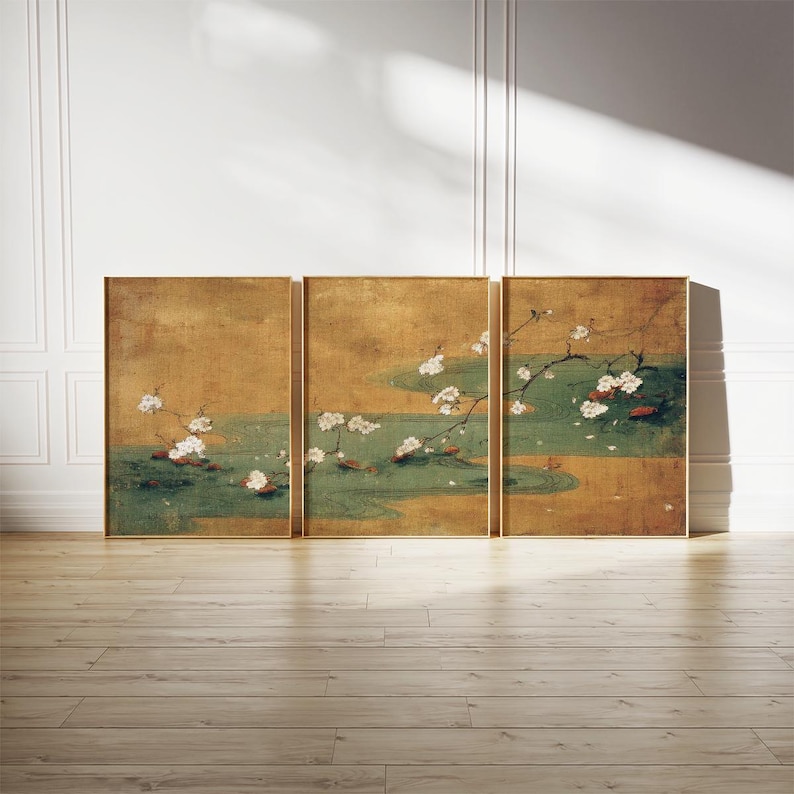 May include: A triptych of framed art panels. Each panel features a gold background with a green and gold water scene. White flowering branches are depicted, with a few red fish. The frames are gold, and the artwork is displayed on a wood floor.