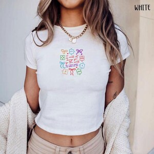 May include: White crop top with a colorful puzzle and bow design. The text reads "I would not change you for the world, but I would change the world for you."