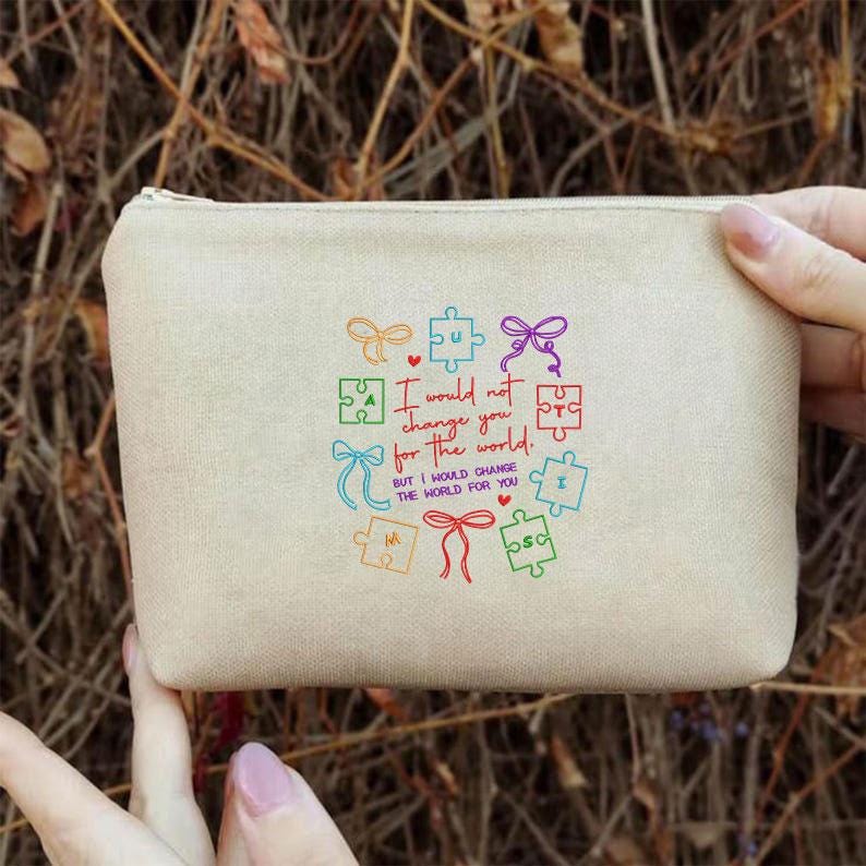 May include: A beige canvas pouch with a zipper closure. The pouch features colorful puzzle pieces and the text "I would not change you for the world. But I would change the world for you."