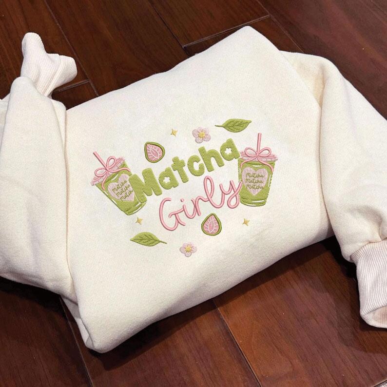 May include: Cream-colored sweatshirt with embroidered "Matcha Girly" design. Features two matcha drink illustrations, leaves, flowers, and a strawberry. The design is in shades of green, pink, and yellow.