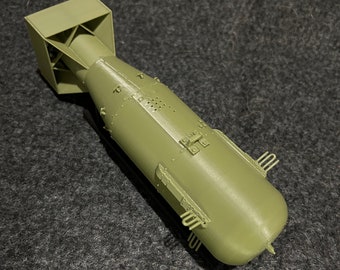 May include: A green model of a large bomb with fins and a tail fin. The bomb has a square-shaped nose and a cylindrical body.