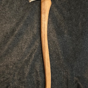 May include: A hand-forged axe with a wooden handle. The axe head is made of steel and has a black finish. The handle is made of wood and has a natural finish. The axe is a traditional tool used for chopping wood.
