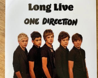 May include: A white sticker with black text that reads "Long Live One Direction". Five young men are pictured in black shirts, standing in a row.