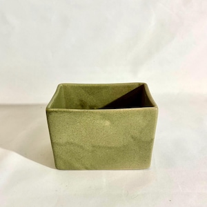 May include: A rectangular ceramic planter with a light sage green speckled glaze. The vessel features a wide, open top with slightly rounded corners and a smooth, matte-textured finish, showcasing a consistent color throughout the exterior surface.