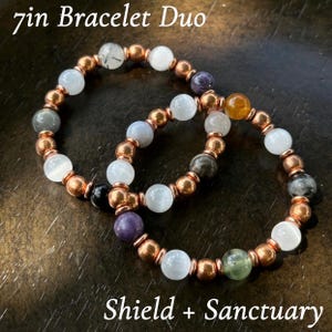May include: Two beaded bracelets, each approximately 7 inches in length, featuring a mix of colorful gemstones and copper-colored metal beads. The bracelets are labeled "7in Bracelet Duo" and "Shield + Sanctuary".