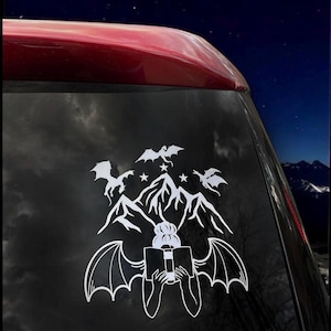 May include: A white vinyl sticker featuring a woman with wings reading a book. The woman is surrounded by mountains and flying dragons. The sticker is perfect for car windows or laptops.