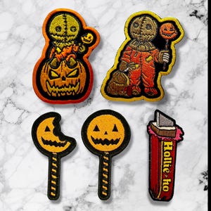 May include: A collection of Halloween-themed embroidered patches. The patches feature a scarecrow figure, jack-o'-lanterns, and lollipops. One patch reads "Hollie-ho". The patches are in orange, black, red, and yellow.