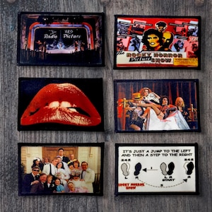 May include: A collection of six rectangular patches featuring imagery from The Rocky Horror Picture Show. The patches include the film's title, iconic lips, a wedding scene, and a dance step diagram. The color palette includes red, black, and white.