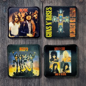 以下が含まれることがあります： ロックバンドのロゴが入った正方形のパッチ4枚。AC/DCのパッチにはバンドメンバーが写っています。Guns N' Rosesのパッチには、スカルの十字架があります。KISSのパッチには、コスチュームを着たバンドメンバーが写っています。Motley Crueのパッチには、バンドメンバーの写真が写っています。すべてのパッチは黒色です。