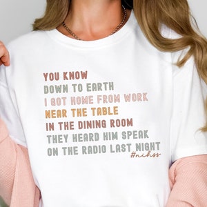May include: White t-shirt with text in various colors: "YOU KNOW DOWN TO EARTH I GOT HOME FROM WORK NEAR THE TABLE IN THE DINING ROOM THEY HEARD HIM SPEAK ON THE RADIO LAST NIGHT #nihss". The shirt is a casual style.