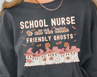 May include: A dark gray t-shirt with the text "School Nurse to all the little friendly ghosts" in white and orange. The shirt features a graphic of seven ghosts wearing witch hats and holding pumpkins.