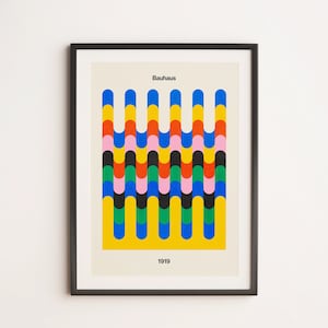 May include: A framed print with a geometric design in a repeating pattern of yellow, blue, red, green, black, and pink. The print has the text "Bauhaus" and "1919" on it.