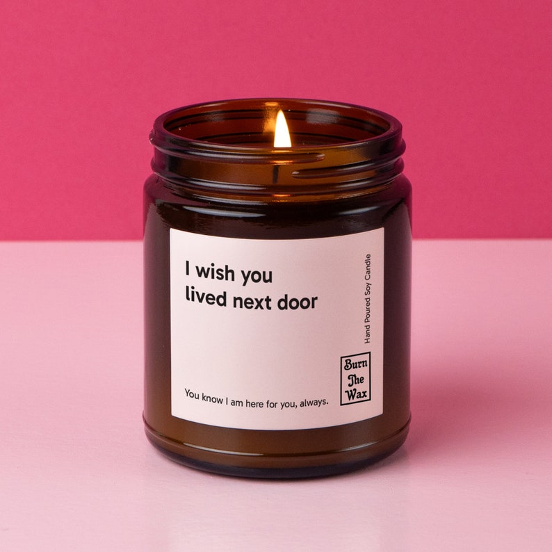 A lit candle in a brown jar with a white label with black text on it