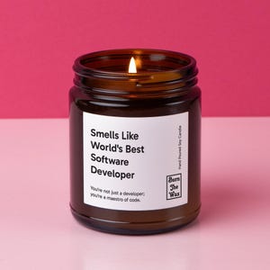 May include: A brown glass candle jar with a white label that reads "Smells Like World's Best Software Developer. You're not just a developer; you're a maestro of code." The label also includes the text "Burn The Wax" and "Hand Poured Soy Candle".