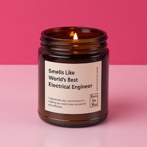 May include: A brown glass candle jar with a soy candle inside. The candle is lit and the jar has a label that reads "Smells Like World's Best Electrical Engineer". The label also includes the text "I appreciate your commitment to making our world more connected and efficient." and the logo "Burn The Wax" with the text "Hand Poured Soy Candle".