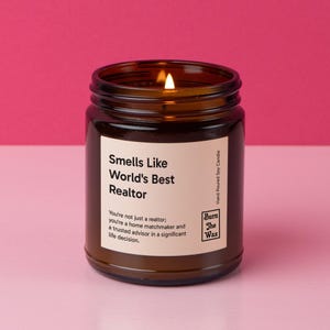May include: A brown glass candle jar with a white label that reads "Smells Like World's Best Realtor". The label also includes the text "You're not just a realtor: you're a home matchmaker and a trusted advisor in a significant life decision." The candle is lit and the label also includes the text "Burn The Wax" and "Hand Poured Soy Candle".