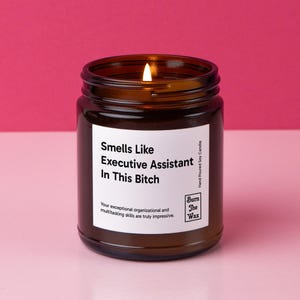 May include: A brown glass candle jar with a white label that reads "Smells Like Executive Assistant In This Bitch". The label also includes the text "Your exceptional organizational and multitasking skills are truly impressive." and the logo "Burn The Wax".