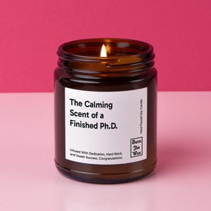 May include: A brown glass candle jar with a white label that reads "The Calming Scent of a Finished Ph.D."  The label also includes the text "Infused With Dedication, Hard Work, and Sweet Success. Congratulations." and the logo "Burn The Wax".