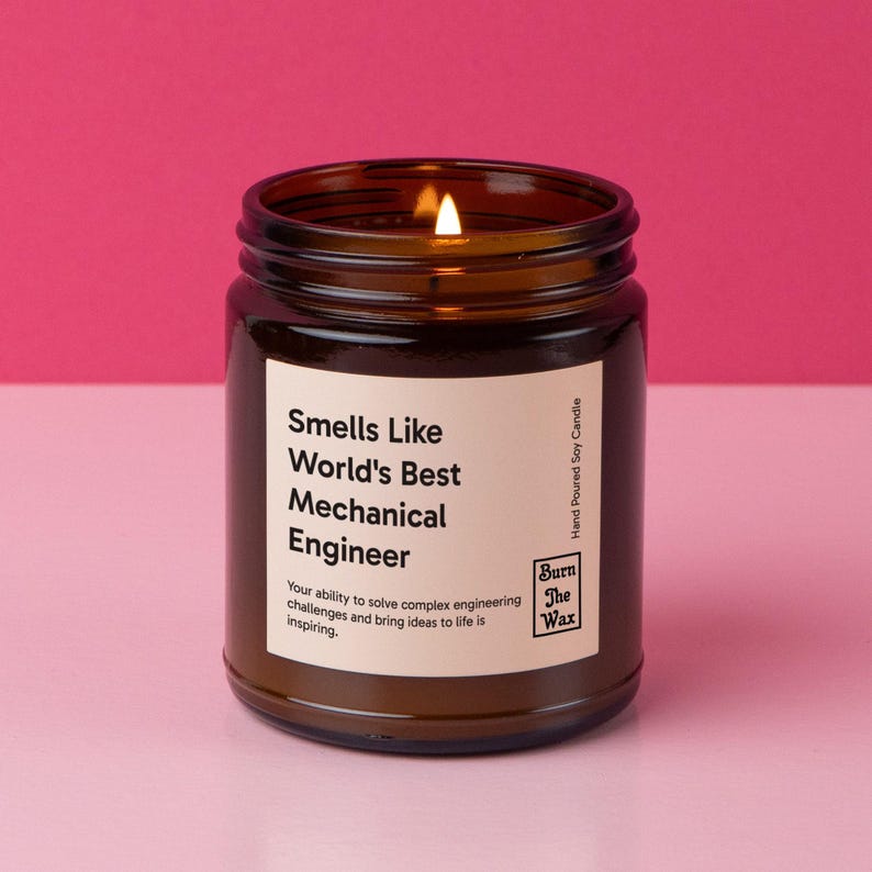 May include: A brown glass candle jar with a white label that reads "Smells Like World's Best Mechanical Engineer". The label also includes the text "Your ability to solve complex engineering challenges and bring ideas to life is inspiring." and the logo "Burn The Wax".
