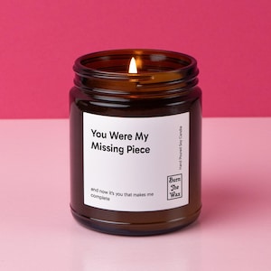May include: A brown glass candle jar with a white label that reads "You Were My Missing Piece and now it's you that makes me complete." The candle is lit and the label also includes the text "Hand Poured Soy Candle" and the logo "Burn The Wax".