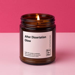 May include: A brown glass candle jar with a white label that reads "After Dissertation Glow". The label also includes the text "Light this candle to celebrate your success and the countless achievements yet to come." and the logo "Burn The Wax" with the text "Hand Poured Soy Candle".