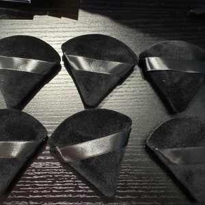 May include: Six black velvet ring boxes with black ribbon accents. The boxes are shaped like cones and are arranged in a semi-circle on a black surface.