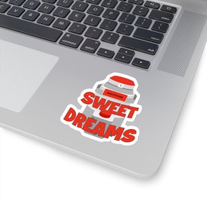 May include: A white sticker with a red and gray design, featuring the words "SWEET DREAMS" in a bold, stylized font. The design includes a red button and the word "HALOTHANE". The sticker is placed on a laptop.
