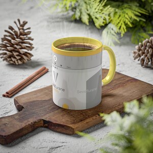 May include: A yellow and gray ceramic coffee mug with the text "Sevoflurane" and a graphic of a medical device. The mug is sitting on a wooden cutting board.
