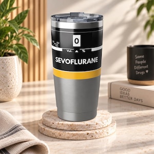 Puede incluir: Un vaso de acero inoxidable con tapa de plástico transparente, que presenta una sección superior negra con el texto SEVOFLURANE, un recuadro blanco con el número 0 y una franja horizontal amarilla sobre una base de color plata cepillada.