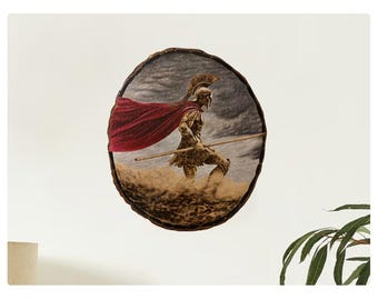 Puede incluir: Una obra de arte redonda de madera que presenta una ilustración detallada de un guerrero espartano con armadura, sosteniendo una lanza y con una capa roja. La obra de arte está ambientada sobre un fondo de cielo tormentoso y terreno arenoso.