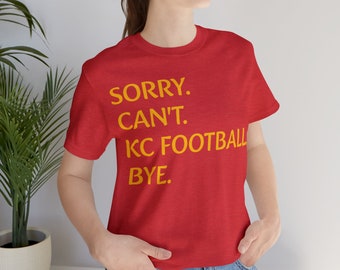 May include: Red t-shirt with the text "SORRY. CAN'T. KC FOOTBALL BYE." in yellow.