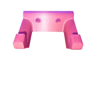 May include: A pink, 3D-printed wall-mounted holder with a rectangular top and two curved arms. The holder has two circular indentations on the top and two angled hooks at the bottom. The object is made of plastic.