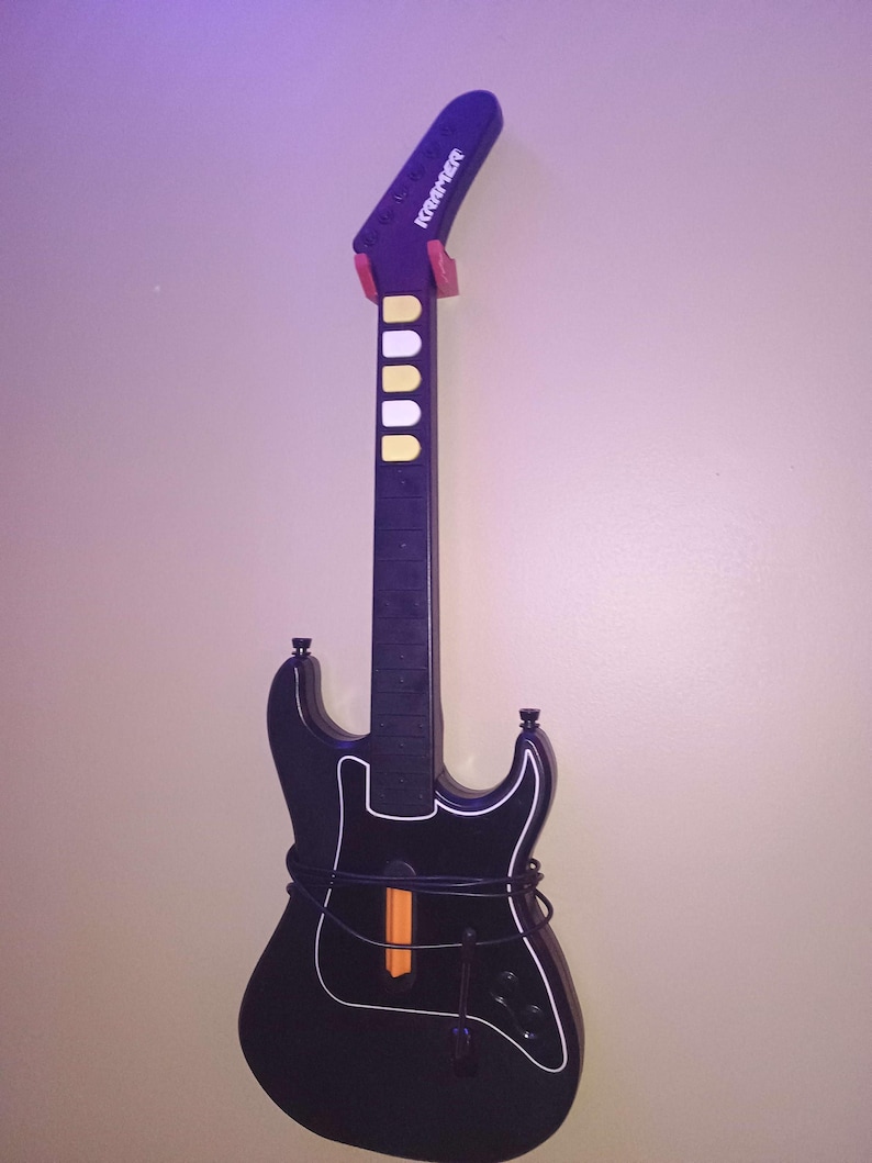 Op de afbeelding: Zwarte gitaarvormige gamecontroller met witte randen en een zwarte hals. De controller heeft een paarse kop met het woord "Kramer" in het wit. Het heeft gele en witte knoppen en een oranje balk.