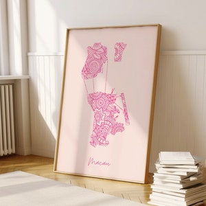 Könnte beinhalten: Ein rosa-weißer Druck der Umrisse von Macau, einer Stadt in China, mit komplizierten floralen Designs. Der Druck ist in einem hellen Holzrahmen gerahmt und hängt an einer weißen Wand.