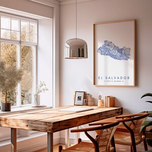 Peut inclure: Une table en bois avec deux chaises dans une pi&egrave;ce avec une fen&ecirc;tre et un luminaire. Une estampe encadr&eacute;e d'El Salvador avec un motif de mandala bleu et blanc est accroch&eacute;e au mur. L'impression comprend le texte "El Salvador 13.2942&deg; N, 88.8965&deg; W".