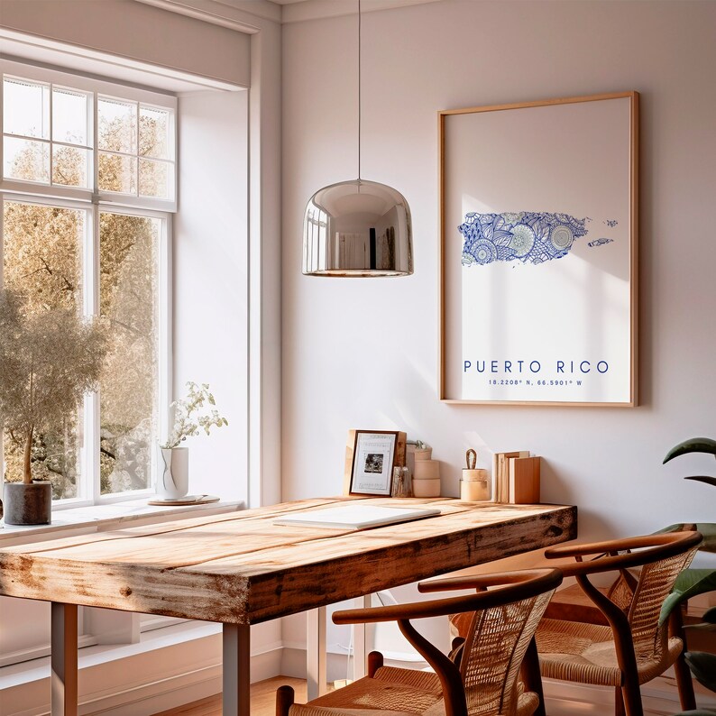 May include: A wooden table with a light wood finish and a metal frame. There is a framed print of a blue and white map of Puerto Rico with the text "PUERTO RICO 18.2208&deg; N, 66.5901&deg; W" on the wall behind the table. There is a silver pendant light hanging above the table.