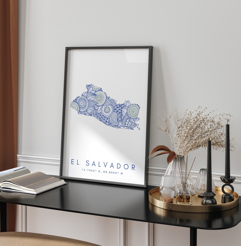 Peut inclure: Une impression encadr&eacute;e en noir avec une carte stylis&eacute;e bleu et blanc du Salvador. La carte est remplie de motifs et de designs complexes. Le texte "EL SALVADOR 13.7942&deg; N, 88.8965&deg; W" est imprim&eacute; sous la carte.