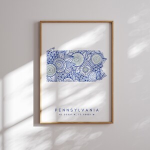 Op de afbeelding: Een ingelijste print van de staat Pennsylvania met een blauw en wit mandala-ontwerp. De print bevat de tekst "PENNSYLVANIA" en de coördinaten "41.2033° N, 77.1945° W".