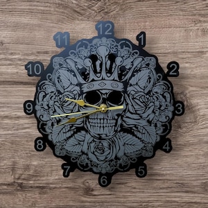 Könnte beinhalten: Schwarze Uhr mit einem Schädel, der eine Krone trägt und von Rosen umgeben ist. Das Zifferblatt der Uhr hat römische Ziffern.