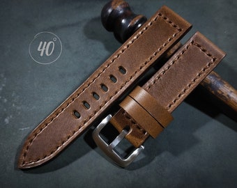 May include: A brown leather watch strap with stitching and a silver buckle. The strap is shown folded in half.