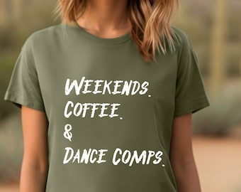 May include: An olive green short-sleeved t-shirt featuring white distressed-style text printed on the front that reads: WEEKENDS. COFFEE. & DANCE COMPS. The shirt has a crew neckline and a standard fit, providing a simple and clear design.