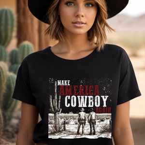 May include: Black t-shirt with a graphic print of two cowboys standing in a desert landscape. The text "Make America Cowboy Again" is printed on the shirt.