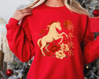 May include: A red sweatshirt featuring a cream-colored horse rearing up, surrounded by red and cream-colored flowers. Chinese characters and a rising sun are also part of the design. The sweatshirt has long sleeves.