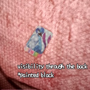 May include: A rectangular, transparent acrylic charm featuring a blue and purple mermaid illustration. The charm has a .5mm hole and is 0.26mm thick. Text on the charm reads "visibility through the back *painted black". The background is pink.